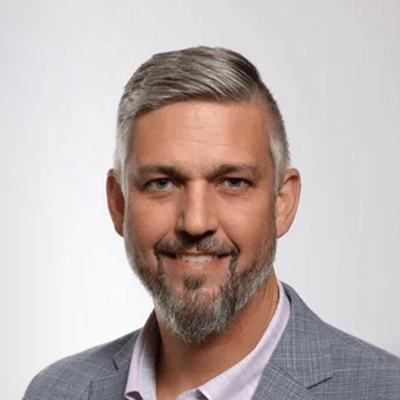 Chiropractor Daniel Atwell Smiling In Suit In Front Of Grey Background